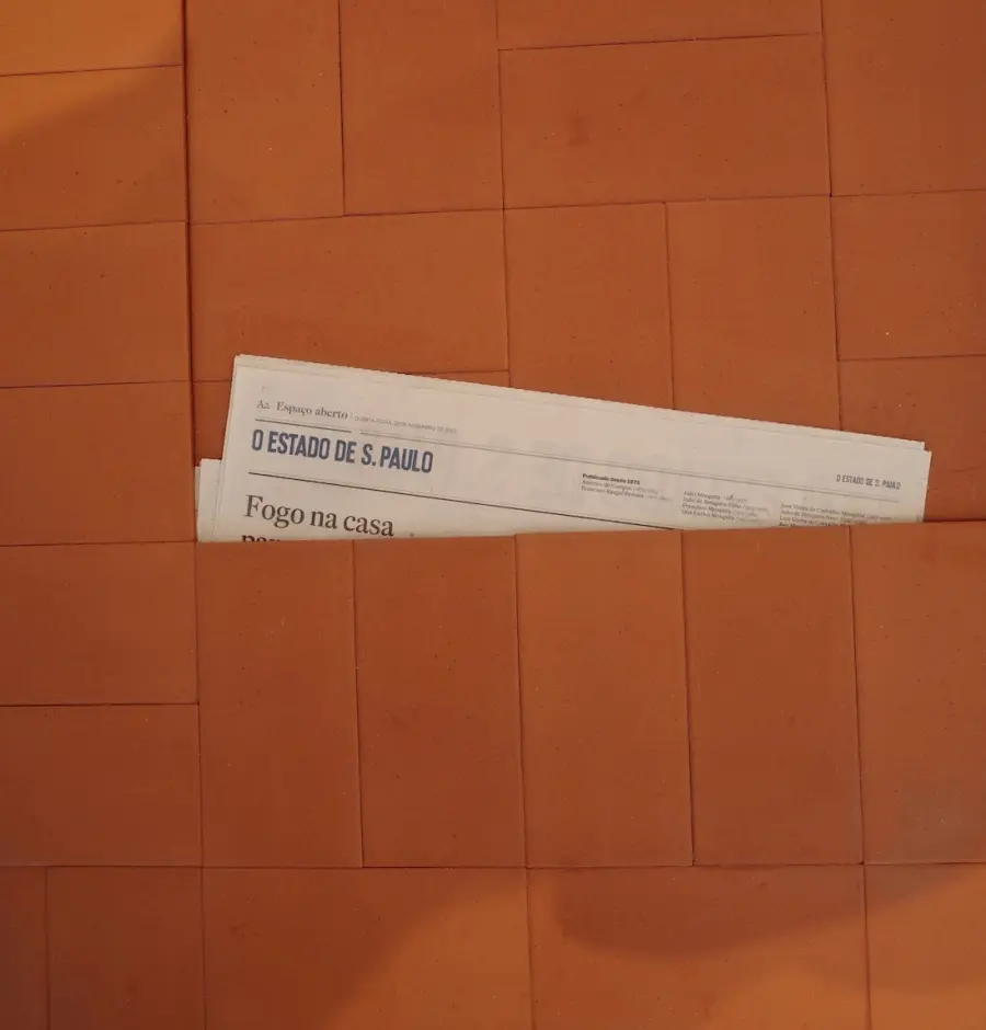 A folded newspaper tucked into a gap in terracotta floor tiles
